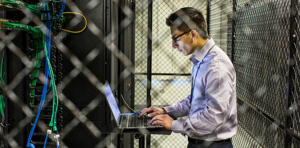 Hispanic man technician doing diagnostic tests on computer servers in a large server farm.